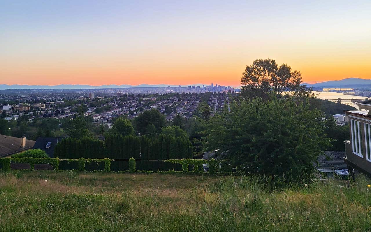 Small green space that overlooks the city of Vnacouver and neighbourhoods with an orange and blue sky of a sunset. A local's favourite spot to watch the sunset from Capitol Hill