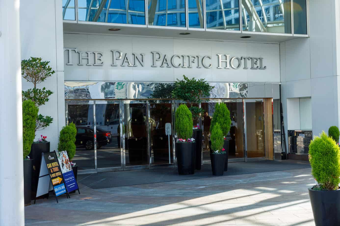 Front of the entrance of the "The Pan Pacific Hotel" glass doors underneath and potted bushes as  decor. The Pan Pacific Hotel has one of the best views from their outdoor pool.